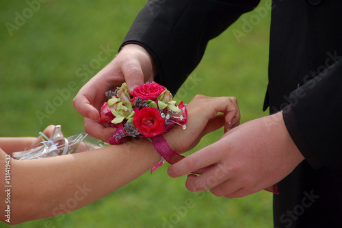 Photo Young man slides wrist corsage onto prom date
