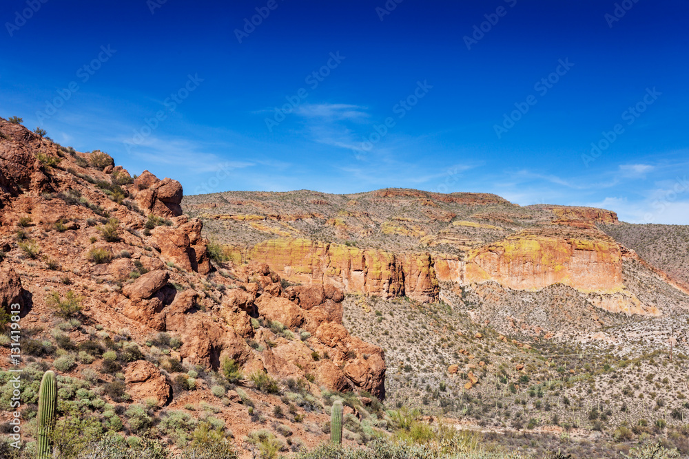 The Apache Trail through the Tonto National Forest has cliffs, saguaro and boulder-strewn hillsides lining the road. The yellow-green areas are lichen growing on the rock face