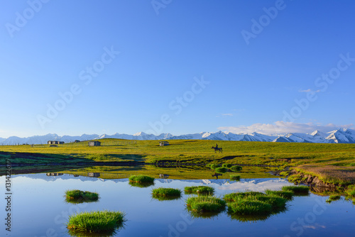 Grassland, snow mountains, wood huts, horse rider, green grasses and blue sky in Xinjiang, China.