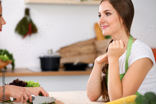 Two women is cooking in a kitchen. Friends having a pleasure talk while preparing and tasting salad. Friends Chef Cook concept