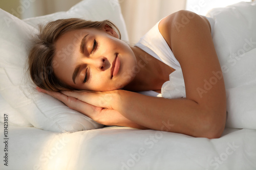 Beautiful young woman sleeping while lying in bed comfortably and blissfully. Sunbeam dawn  on her face