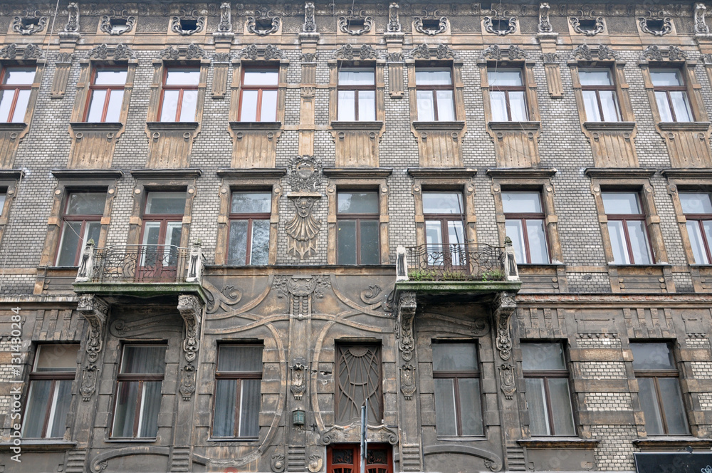 Facade of the old multistory buildings in Art Nouveau style. Dirty walls and rows of windows with decorative elements. Krakow, Poland.
