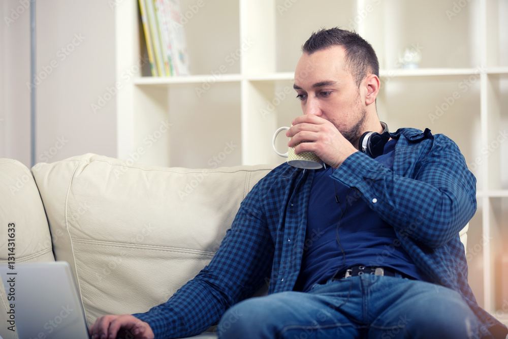 Handsome man sitting on sofa with laptop drinking tea Handsome man sitting on sofa with laptop drinking tea