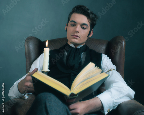 Retro victorian dickens style man reading book by candlelight. photo