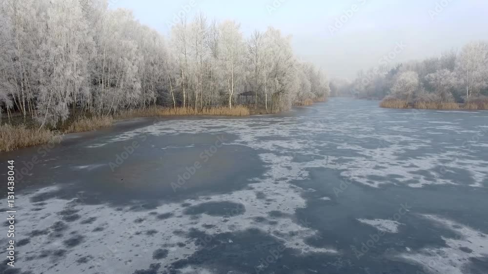 Aerial view of the winter background with a snow-covered forest and lake from above captured with a drone in Poland.
