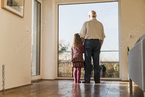 Grandfather and granddaughter looking out of window, rear view photo