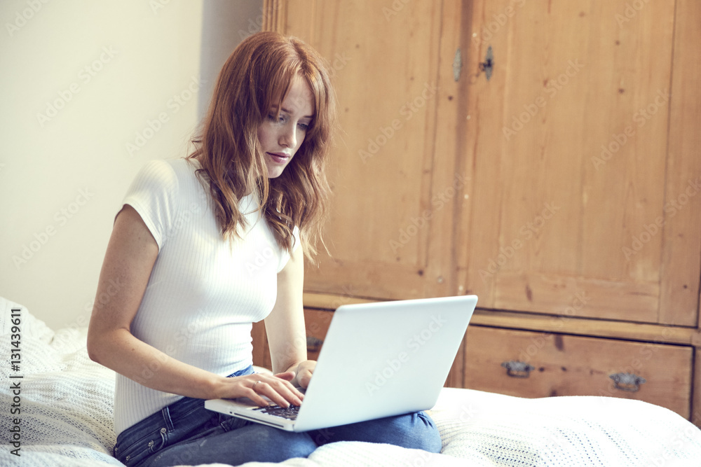 Redheaded woman sitting on bed using laptop Redheaded woman sitting on bed using laptop
