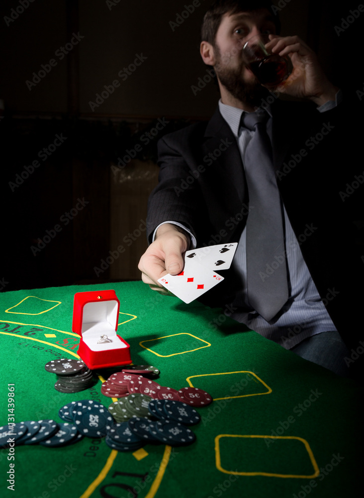 gambling addiction. man in a business suit drinking brandy and throws cards with losing combination. casino chips, precious ring on green poker table gambling addiction. man in a business suit drinking brandy and throws cards with losing combination. casino chips, precious ring on green poker table