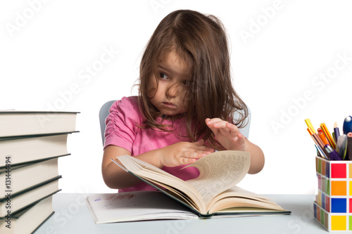 Small girl in pink t-shirt learning how to read at her desk and worried about how much she has to read