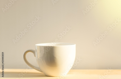 White coffee cup placed on a wooden floor with a white background and soft light