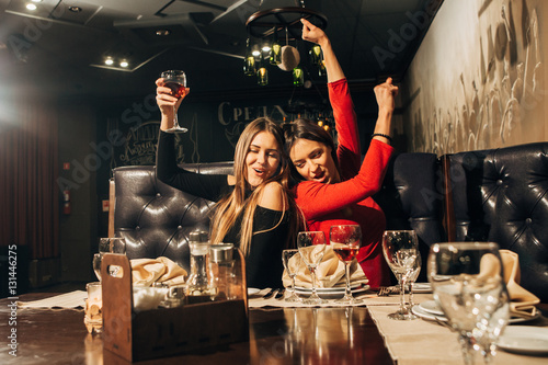 Two beautiful happy women having fun in a bar drinking wine