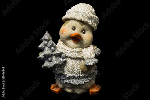 cute ceramic figure of penguin in knitted clothes with small pine tree, cristmas toy on black background