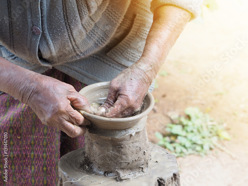 Old woman's hands sculpt clay pottery on wooden stand.