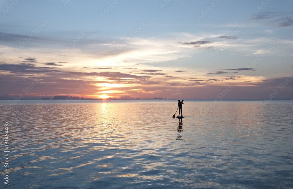 Silhouette of woman on paddle board at sunset.
