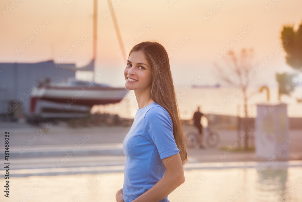 candid portrait of a beautiful young woman smiling, while on a sunset background by the sea
