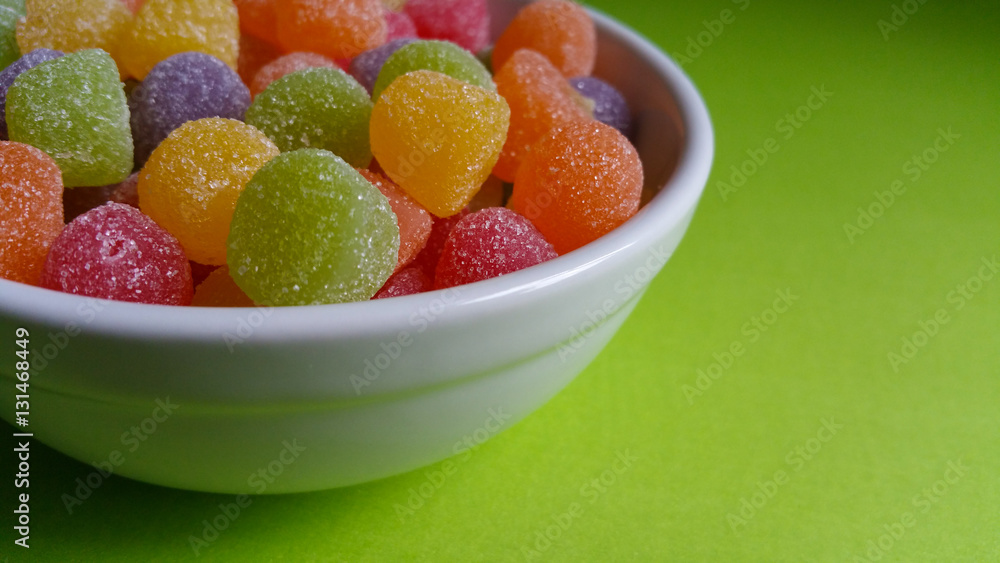 Colored jelly beans in white pot with green background Colored jelly beans in white pot with green background