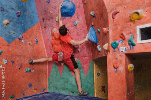 Rear view of a young man practicing in climbing at artificial wall in gym