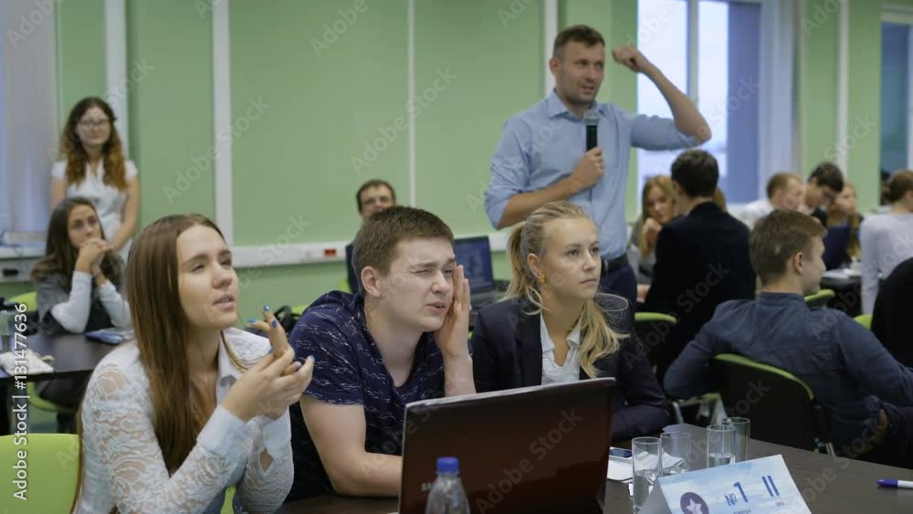 Team of young entrepreneurs sitting at the desk with laptop and preparing to make presentation of their new Internet startup to the audience, while speaker Team of young entrepreneurs sitting at the desk with laptop and preparing to make presentation of their new Internet startup to the audience, while speaker