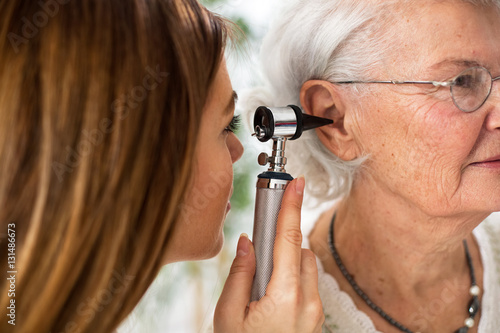 Doctor holding otoscope and examining ear of senior woman photo