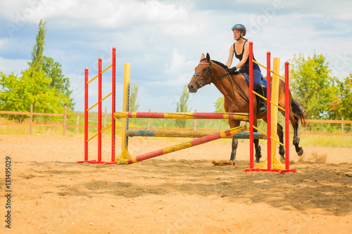 Jockey young girl doing horse jumping through hurdle