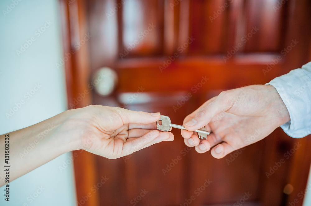 Man's hand gives a key female  on  background of  wooden door. Deal with the real estate concept