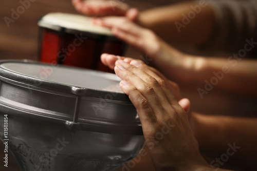 Hands of man playing African drum on brown blurred background, close up