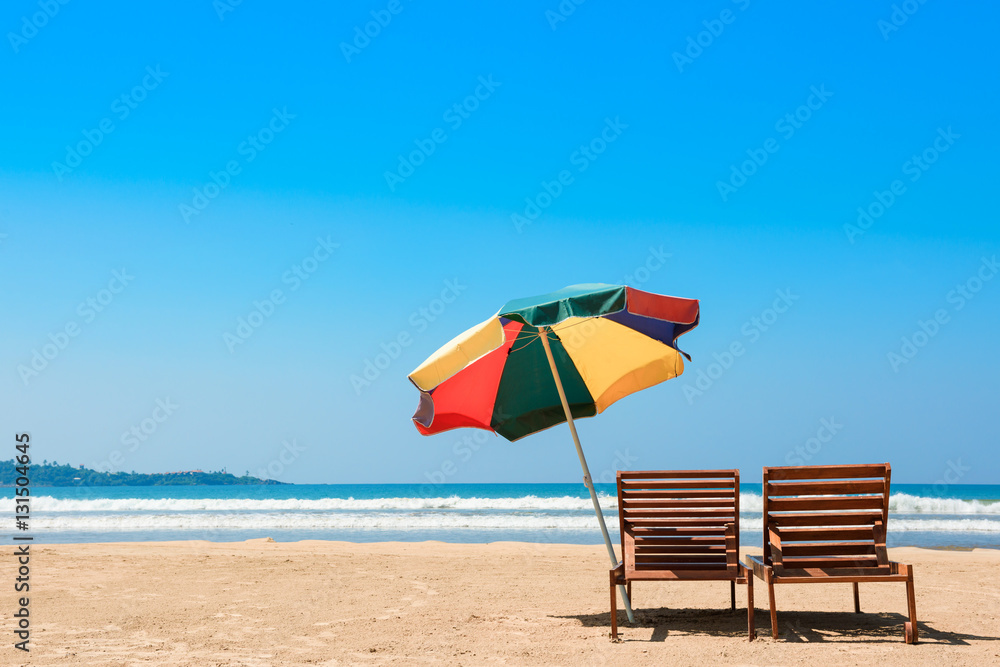 Two beach chairs and umberella on tropical ocean beach at sunny day