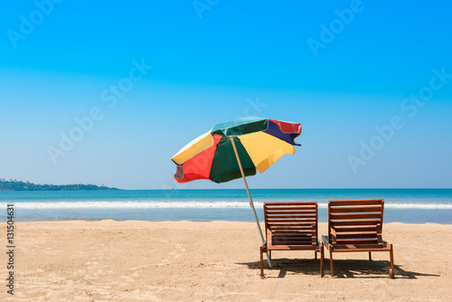 Two beach chairs and umbrella on tropical ocean beach at sunny day