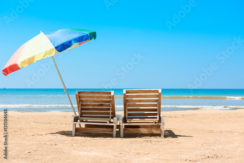 Two wooden beach chairs and umbrella on tropical ocean beach at sunny summer day