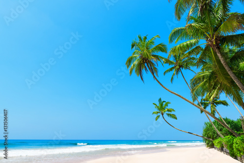 Fototapeta Naklejka Na Ścianę i Meble -  Beautiful tropical beach with coconut palm trees, idyllic clean ocean white sand and clear blue sky at sunny summer day on luxury remote resort