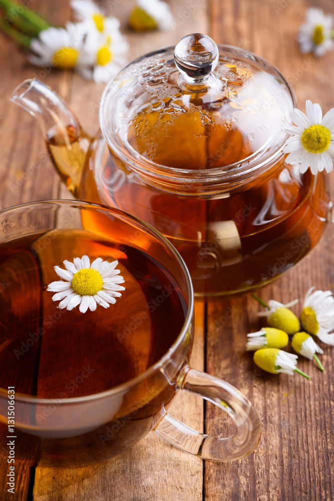 Herbal chamomile tea in cup and glass teapot with fresh chamomile herbs on vintage wooden table background Herbal chamomile tea in cup and glass teapot with fresh chamomile herbs on vintage wooden table background