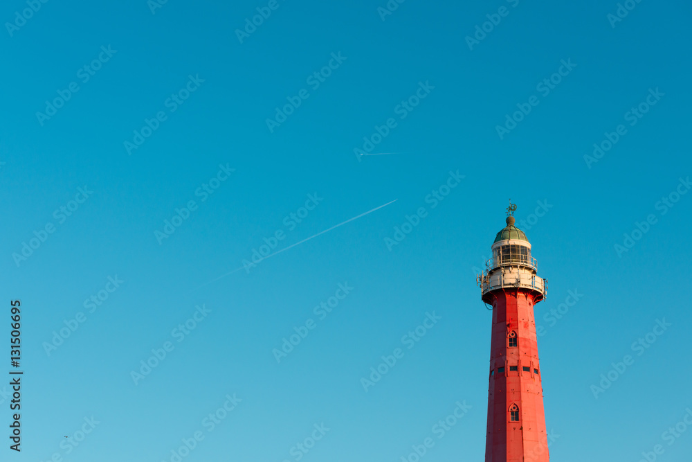 Lighthouse over blue sky background with airplane traces and copy space