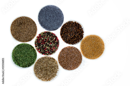 Herbs and seasonings - dried coriander, peppercorn, flax seeds, mustard, clove, cumin, parsley and poppy seeds in a transparent dish isolated on white background.