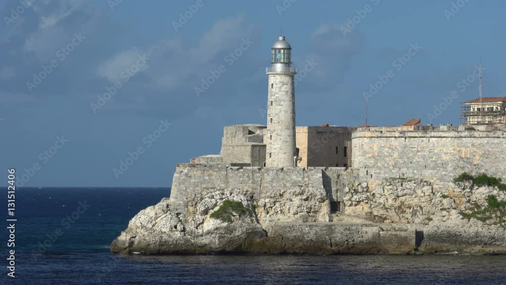 Close-up view on big stone lighthouse into sea bay which is placed in fortress at downtown of Havana. People are walking by seafront. Close-up view on big stone lighthouse into sea bay which is placed in fortress at downtown of Havana. People are walking by seafront.