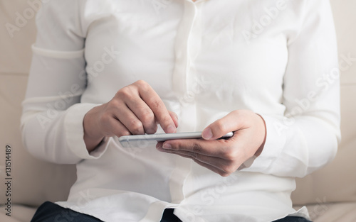 woman is sitting on a sofa and using a smartphone