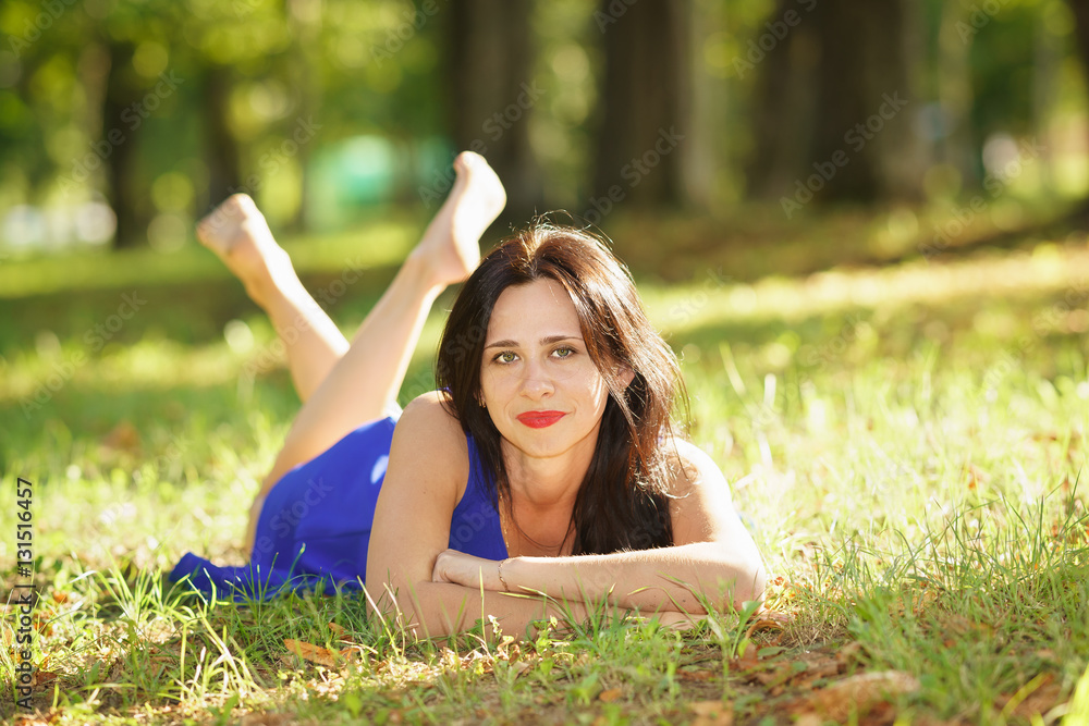 Beautiful young woman smiling in blue dress lying on the grass Beautiful young woman smiling in blue dress lying on the grass