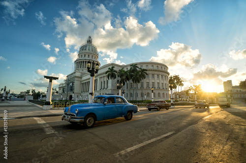 Blue retro car is riding near ancient colonial Capitol building at the center of Havana at sunset  © simonovstas