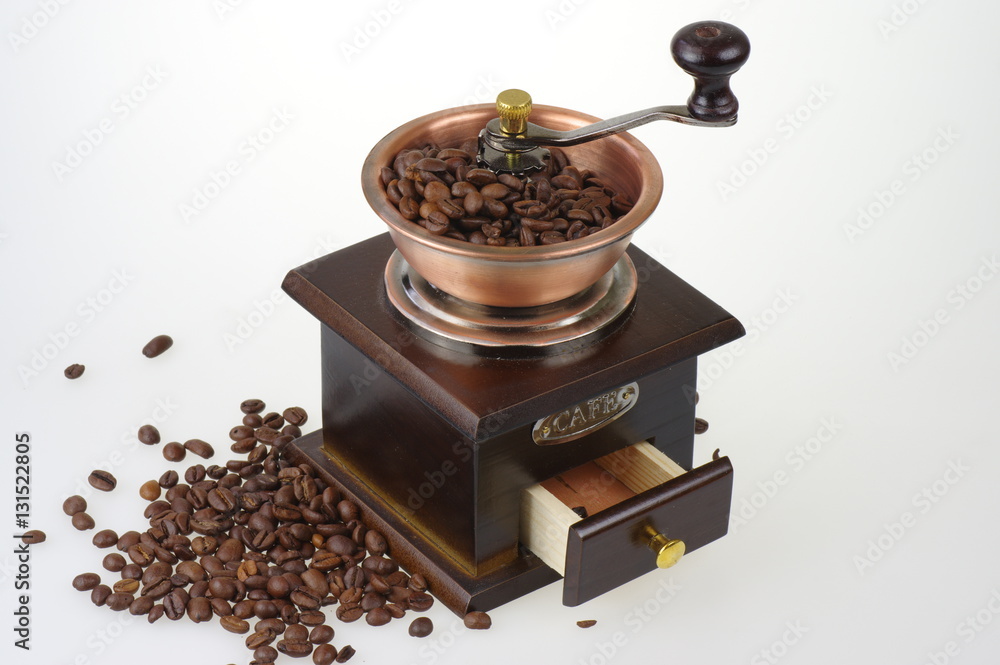 Old-style manual coffee grinder on the white background. Around the mill are scattered coffee beans. Old-style manual coffee grinder on the white background. Around the mill are scattered coffee beans.
