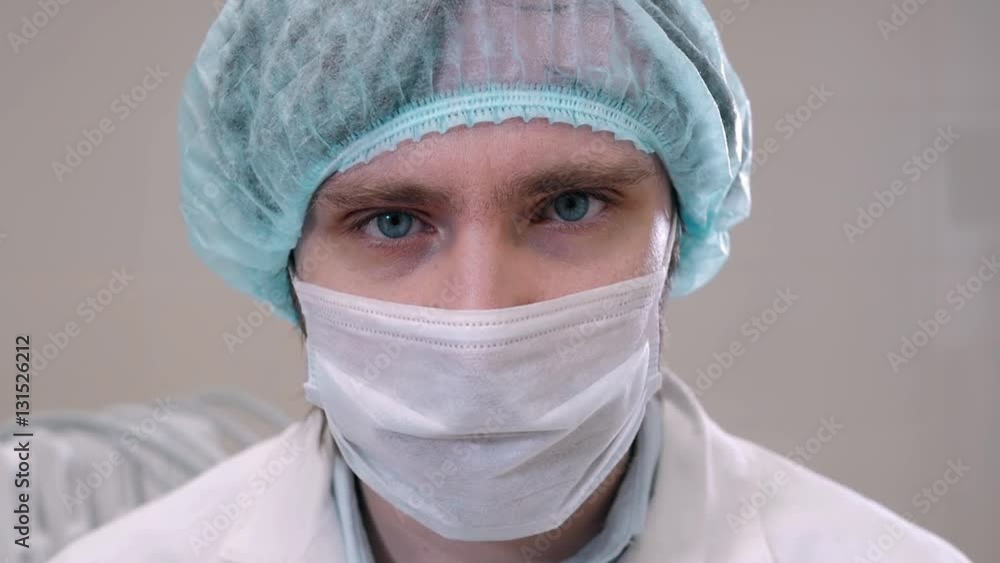 Handsome surgeon in mask is looking at camera, standing in a modern operating room, close up, patient in clinic, coronavirus pandemic, quarantine Handsome surgeon in mask is looking at camera, standing in a modern operating room, close up, patient in clinic, coronavirus pandemic, quarantine