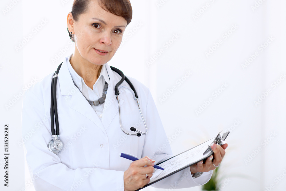 Happy female doctor standing in hospital and filling up medical form. Medicine and health care concept. Happy female doctor standing in hospital and filling up medical form. Medicine and health care concept.
