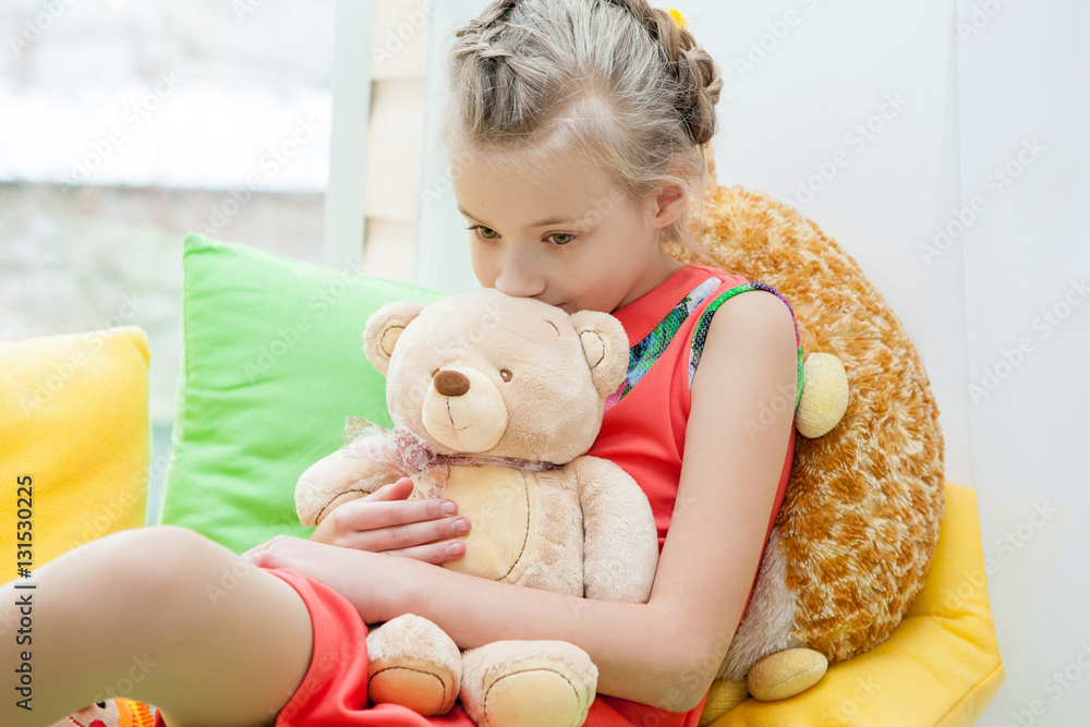 Thoughtful Little girl with toy bear sits on window Thoughtful Little girl with toy bear sits on window