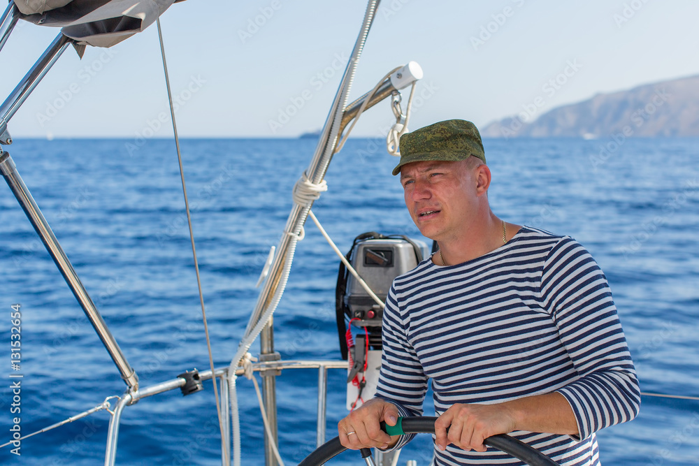 Young man at the helm on the sailing boat. Ship controls during sea yacht race.