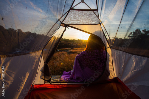 women sit front of camping tent glow up with sunrise in morning