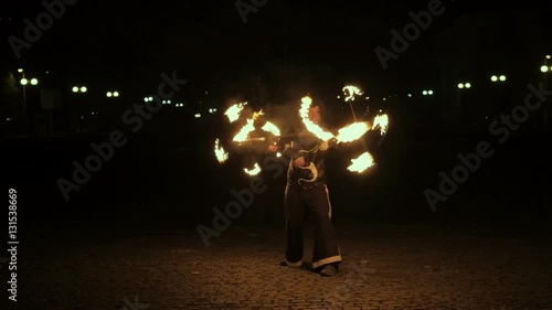 Fire show performance. Handsome male fire juggler performing contact manipulation with fire baton with several wicks ?? dragon staff. Close-up. Slow motion photo