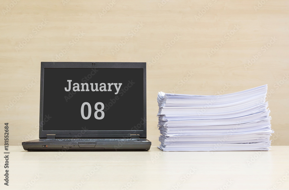 Closeup computer laptop with january 8 word on the center of screen in calendar concept and pile of work paper on wood desk and wood wall in work room textured background with copy space Closeup computer laptop with january 8 word on the center of screen in calendar concept and pile of work paper on wood desk and wood wall in work room textured background with copy space