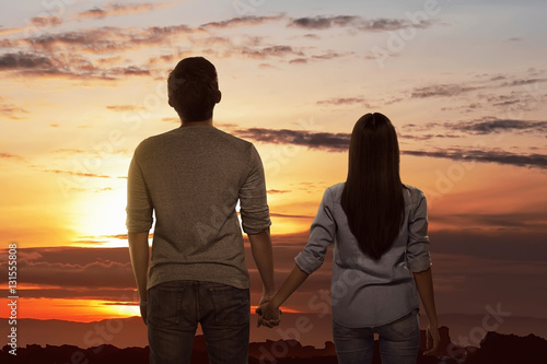Romantic asian couple holding hands looking sunset