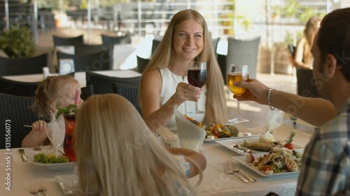 Family with kids clink glasses in outdoor restaurant