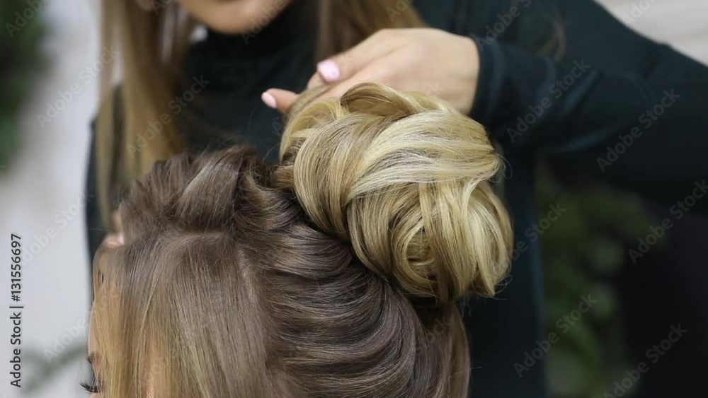 Hairdresser creating complicated evening and wedding hairstyles at barbershop salon. Close-up of hands corrects hair curls and strands