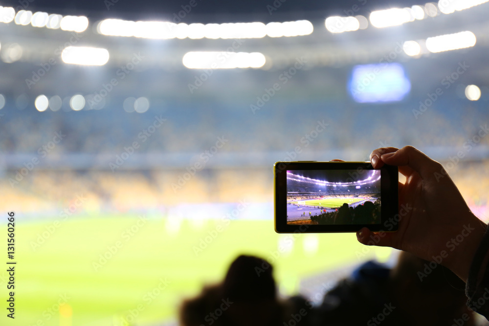 Fototapeta premium Fan taking video of football game at stadium