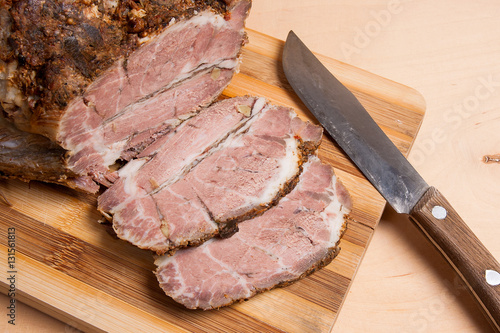 Sliced baked pork with herbs and spice on wooden board.